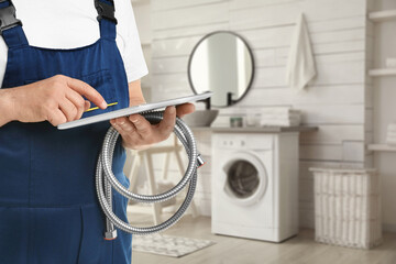 Plumber with shower hose and tablet in bathroom, closeup. Space for text