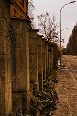 Ogrodzenie z cegły , kamienia ( piaskowiec ) oraz stalowych prętów , biegnące wzdłuż ulicy z latarniami wczesną wiosną . - obrazy, fototapety, plakaty