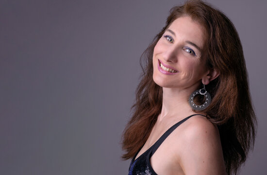 Primer plano de mujer cauc&aacute;sica de cabello casta&ntilde;o en actitud positiva y sonriente, sobre fondo lila y predominio de tonos azulados  