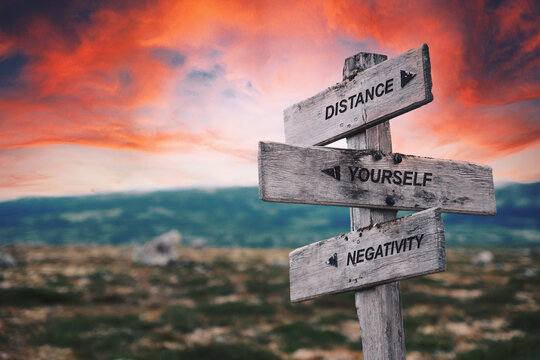 distance yourself negativity quote caption text written engraved on wooden signpost outdoors in nature with dramatic red skies.