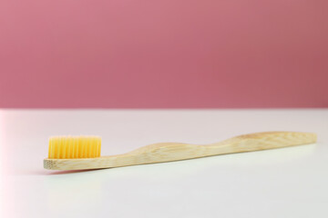 Bamboo eco toothbrush on a white table and pink background. Space for text. The concept of ecology, biodegradable substances