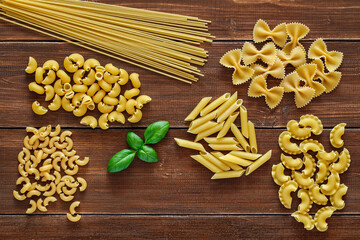 Pasta, set of raw farfalle, spaghetti, pipe rigatoni, maccheroni, penne rigate, cresta di gallo, basil leaf,  on wooden plank dark background, top view, space to copy text.