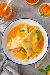 Delicious crepes suzette with orange syrup and slices fruits on a plate on a gray concrete background, top view