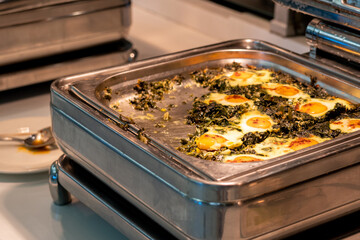All-inclusive buffet food in heating trays in hotel restaurant with eggs with spinach for breakfast