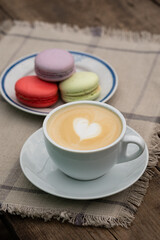 Cup of cappuccino with colorful macaroons on a wooden table