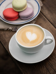 Cup of cappuccino with heart and colorful macaroons on a wooden table