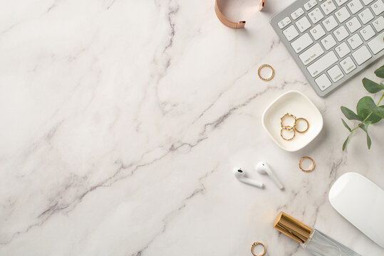Business concept. Top view photo of workstation keyboard computer mouse wireless earbuds gold rings bracelet perfume bottle and eucalyptus on white marble background with copyspace