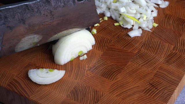 Chef cuts fresh onions with old knife into pices on wooden cutting board. Preparation of ingredients