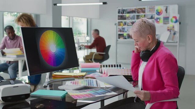 Senior illustrator sitting at desk choose colors for book or magazine cover