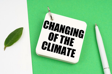 On a white-green surface, a piece of paper, a pen and a notepad with the text - Changing of the climate