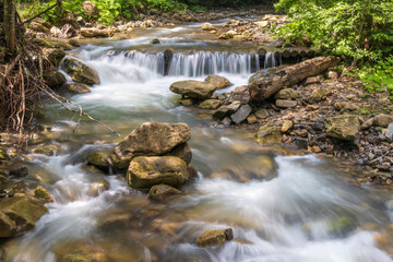 Fototapeta na wymiar wide forest creek with stones in long exposure