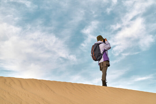 asian woman photographer taking a photo on top of a sand dune