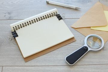 open notebook with a spiral near an envelope and a magnifying glass