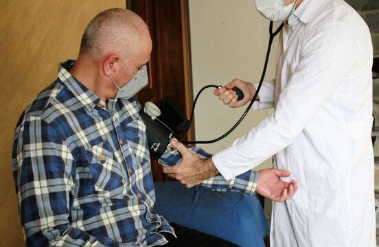 Médico accionando tensiómetro para medir presión arterial en paciente adulto