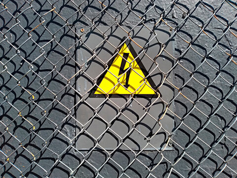 electrical hazard sign placed on an electric power substation behind a metal fence of wire mesh, sanctions, restrictions