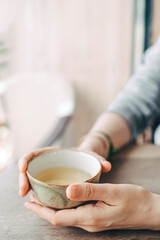 Women's hands hold a cup of tea at a table in a cafe.