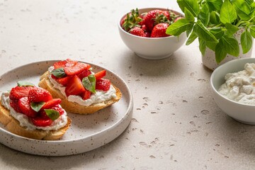 Bruschetta with ricotta, strawberries and basil on light background. Comfort food. Copy space. Selective focus.