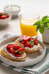 Homemade bruschettas with strawberries, cream cheese and basil in white plate on light background. Summer appetizer. Selective focus.