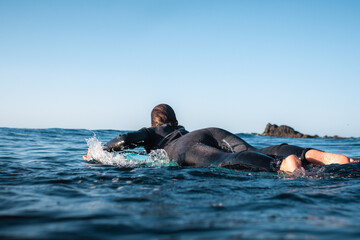 Surfer girl seen from behind. Paddling on a board in the water