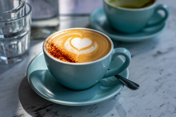 Latte or Cappuccino Coffee with foam latte art heart shape on top in cafe with strong shadows
