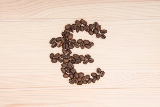 Wooden craft surface as a comfortable background wall or floor with different structures of light wood full of many coffee beans . A Euro sign shaped coffee beans. Situated at the middle of the table.