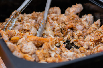 Cooked roasted golden brown chicken meat pieces in black food container on table at summer local food market - close up view. Outdoor cooking, gastronomy, cookery, street food concept