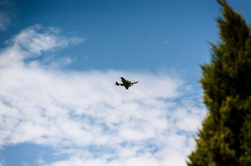 A large military supersonic fighter plane with missiles flies low in the blue sky with clouds.