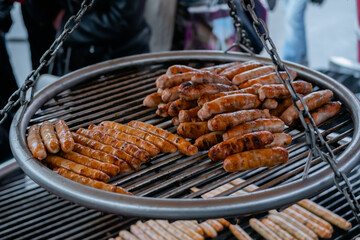 Process of grilling fresh meat sausages on big round hanging grill at summer local food market. Outdoor cooking, barbecue, gastronomy, cookery, street food concept