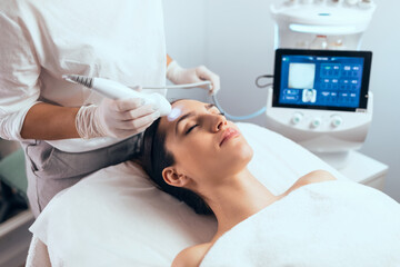 Cosmetologist making ultrasonic cleaning and rejuvenation the face to beautiful woman on the spa...