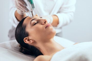 Cosmetologist making ultrasonic cleaning and rejuvenation the face to beautiful woman on the spa...