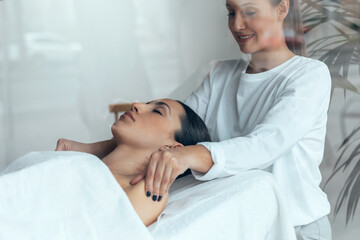 Cosmetologist making relax massage to beautiful woman while lying on a stretcher in the spa center.