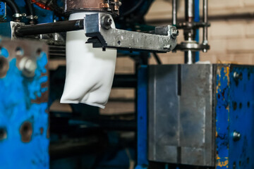 The process of blowing plastic tanks and canister in extrusion equipment. Molten white plastic like a tube is placed in a press form and blowing the air and is give to shape of the bottle