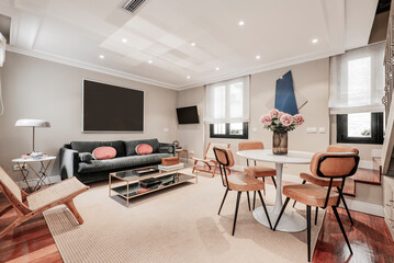 Living room with round white dining table with chairs upholstered in tobacco-colored leatherette, three-seater armchair upholstered in green velvet and side table with mirrors