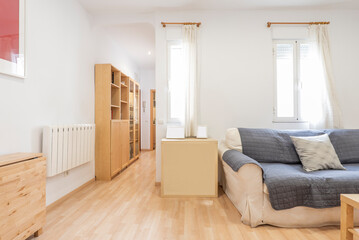 Living room with folded wooden dining table, two-seater sofa, various wooden furniture, TV on chest of drawers and corridor with shelves and windows with curtains
