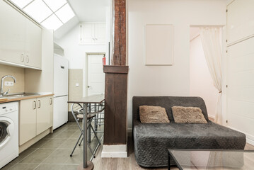 Studio apartment with furnished living room and open kitchen with cream cabinets and wooden countertops, vintage wooden columns and skylight in the sloping ceiling