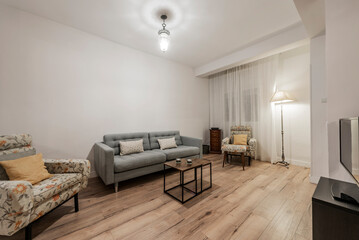 Apartment with a living room with black metal and wood side tables, a three-seater sofa and armchairs with flowers and a light wooden floor