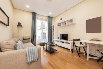 Apartment with a living room with a square white folding dining table, white wooden furniture, black metal side tables, a three-seater sofa and a light wooden floor