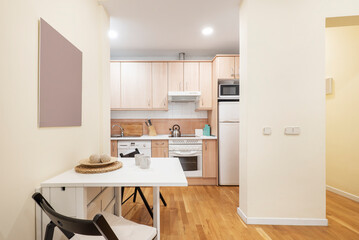 Apartment with open kitchen, living room with square white folding dining table and light wooden floor