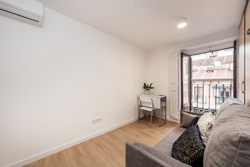 Living room with white folding table in a corner, sofa bed and vintage wooden balcony with city views