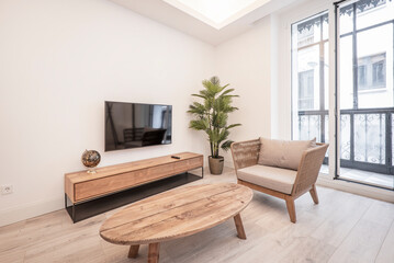 Corner of a living room with a wooden side table, an elongated sideboard with drawers and a balcony with metal and glass