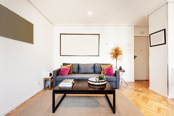 Living room with three-seater sofa in blue fabric, side table in dark wood, rattan rug and herringbone oak parquet floors