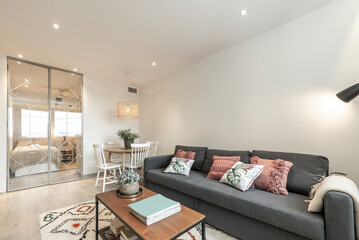 Living room with large sofa bed with cushions, wood and metal side table and glass and metal doors