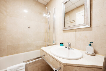 Bathroom with cream marble walls, countertop of the same material, white porcelain sink and mirror with silver frame