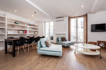 Studio apartment with long black wooden dining table and matching chairs with resin seats, wall-to-wall plaster shelving and large balconies with street views