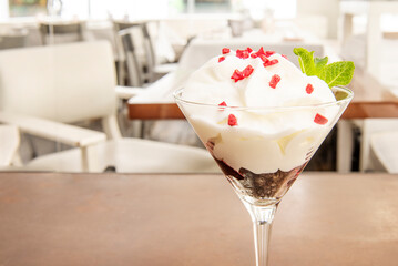 Cup of creamy yogurt with strawberry chips and dark chocolate background on the table of an empty restaurant