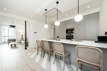 Kitchen with tall marble island with raw wood chairs, gray cabinets and globe lamps