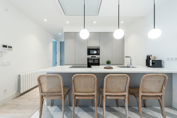 Marble kitchen island with raw wood chairs, gray kitchen cabinets, built-in appliances, mixed wood flooring and globe lamps