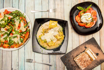 Italian food dishes with pasta, burrata salad with tomato and olive oil and Neapolitan pizza with arugula, parmesan cheese, cherry tomatoes and tiramisu for dessert