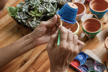 Hands of a Latin woman, painting clay pots to plant succulent plants