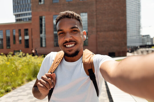 Happy young man taking selfie picture in earbuds walking outdoors
